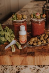 pique bottle in between olives on top of a wooden cutting board