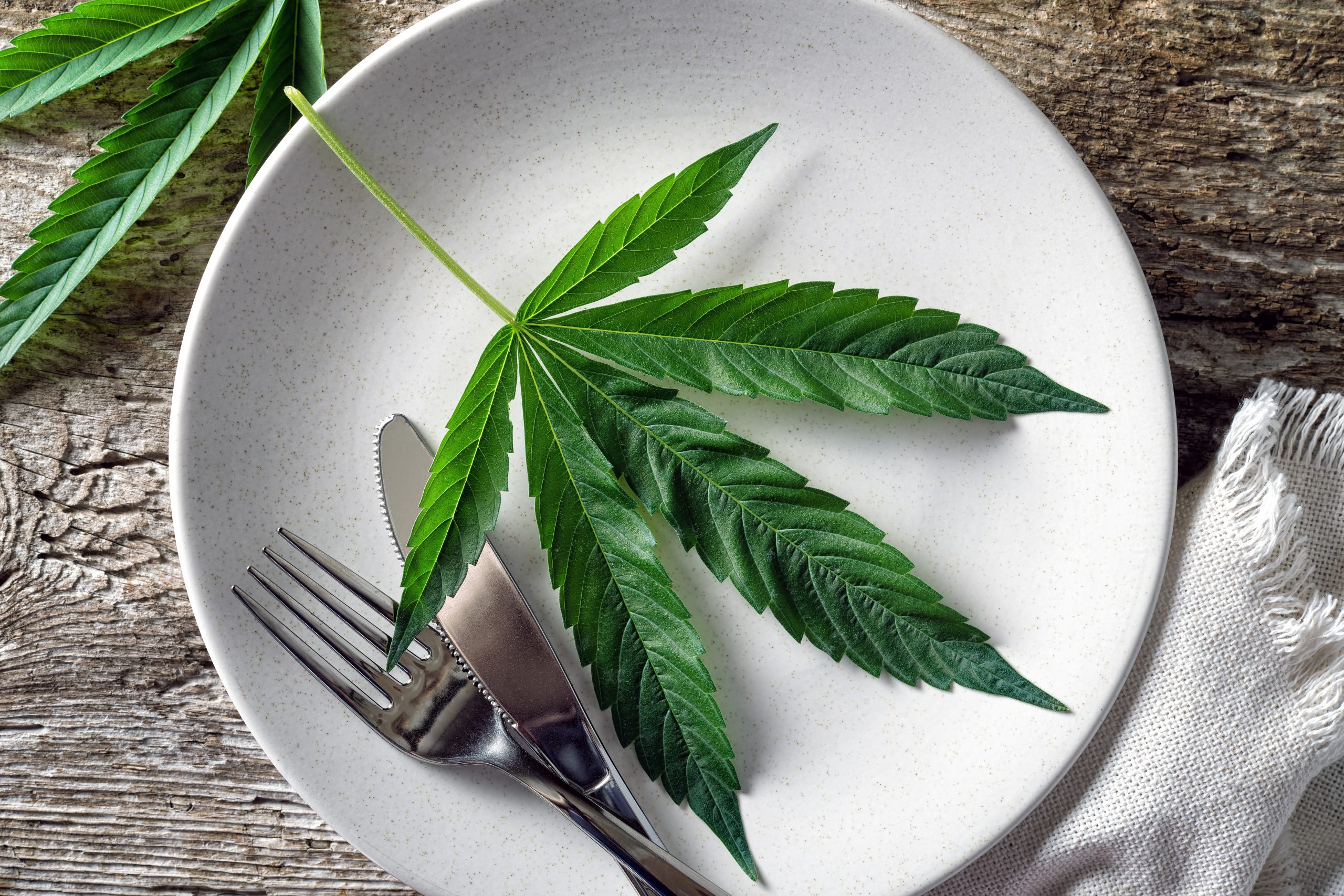 Conceptual image of a cannabis leaf on a plate with a knife and fork.